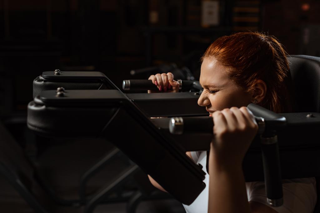 purposeful overweight girl doing arms extension exercise on fitness machine - Photo, Image