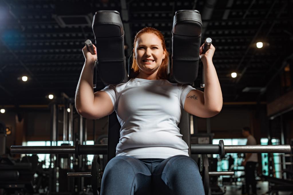 levágott kilátás céltudatos túlsúlyos lány csinál kar kiterjesztése gyakorlat fitness gép - Fotó, kép