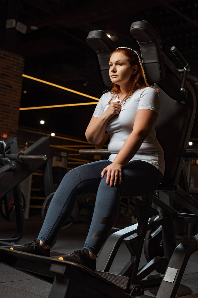confiante menina com sobrepeso olhando embora enquanto sentado na máquina de fitness
 - Foto, Imagem