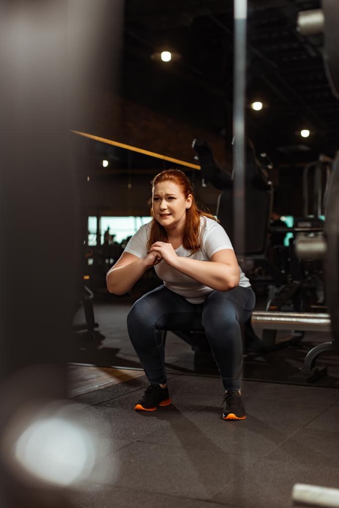 selective focus of overweight girl squatting with clenched hands in gym - Photo, Image