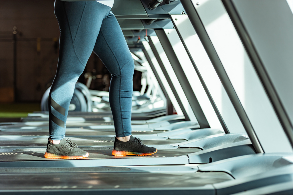 cropped view of overweight girl in leggings running on treadmill in gym - Photo, Image