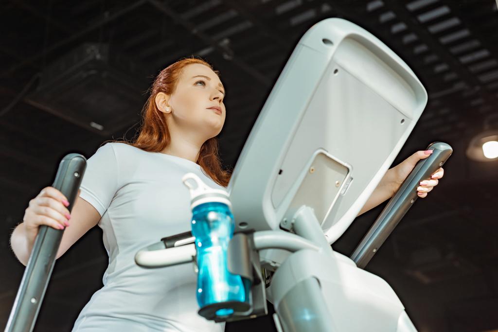 low angle view of focused overweight girl working out on stepper in gym - Photo, Image
