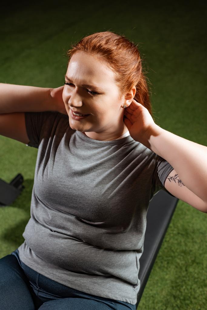 hoge hoek uitzicht van doelbewust overgewicht meisje doen buikspieroefeningen op fitnessapparaat  - Foto, afbeelding