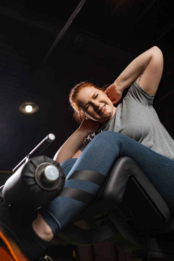 Düşük açılı, kaslı, kilolu bir kızın fitness makinesi üzerinde karın kası egzersizi yapması.  - Fotoğraf, Görsel
