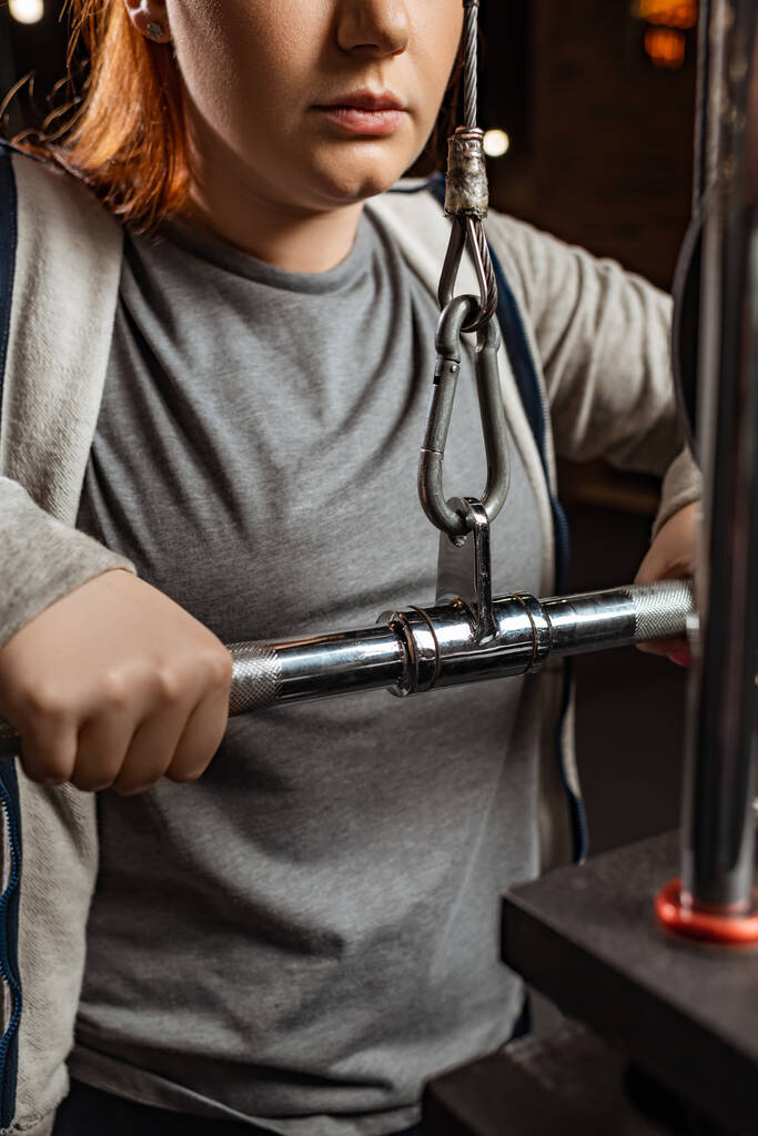 περικοπή άποψη του υπέρβαρου κορίτσι κάνει την επέκταση των όπλων άσκηση στο μηχάνημα γυμναστικής - Φωτογραφία, εικόνα