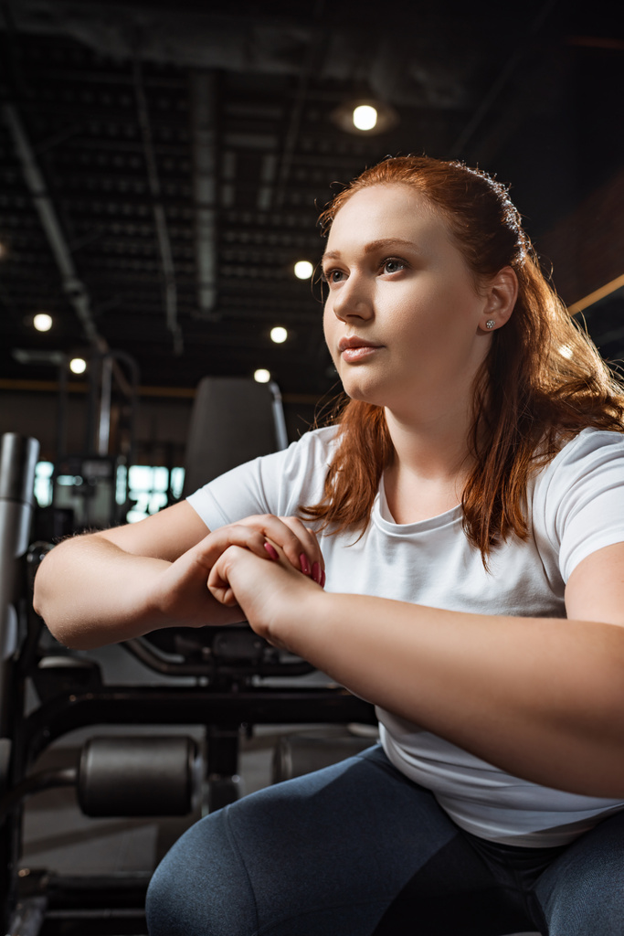 уверенная девушка с избыточным весом, приседающая с сжатыми руками в спортзале
 - Фото, изображение