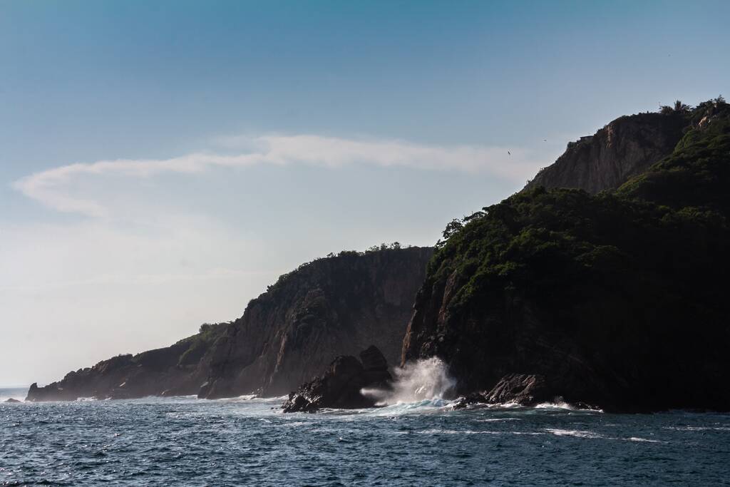 Arka planda mavi bir gökyüzü ile kayalıklara vuran güçlü deniz dalgalarının güzel bir görüntüsü. - Fotoğraf, Görsel