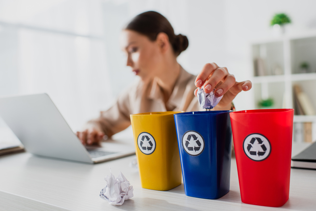 selectieve focus van zakenvrouw gooien verfrommeld papier in recycling emmers tijdens het werken op laptop  - Foto, afbeelding