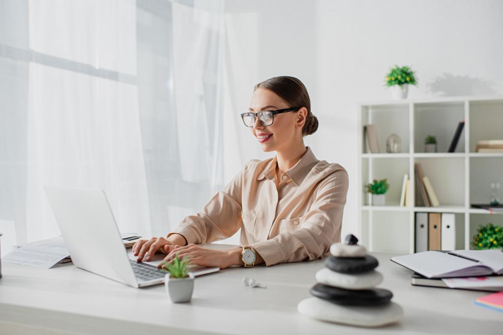 souriant femme d'affaires travaillant avec ordinateur portable sur le lieu de travail avec des pierres zen
 - Photo, image