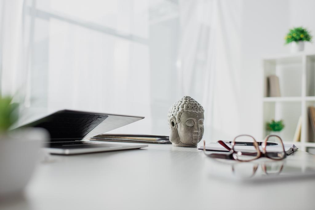 Buddhakopf, Brille und Laptop auf dem Tisch im modernen Büro - Foto, Bild