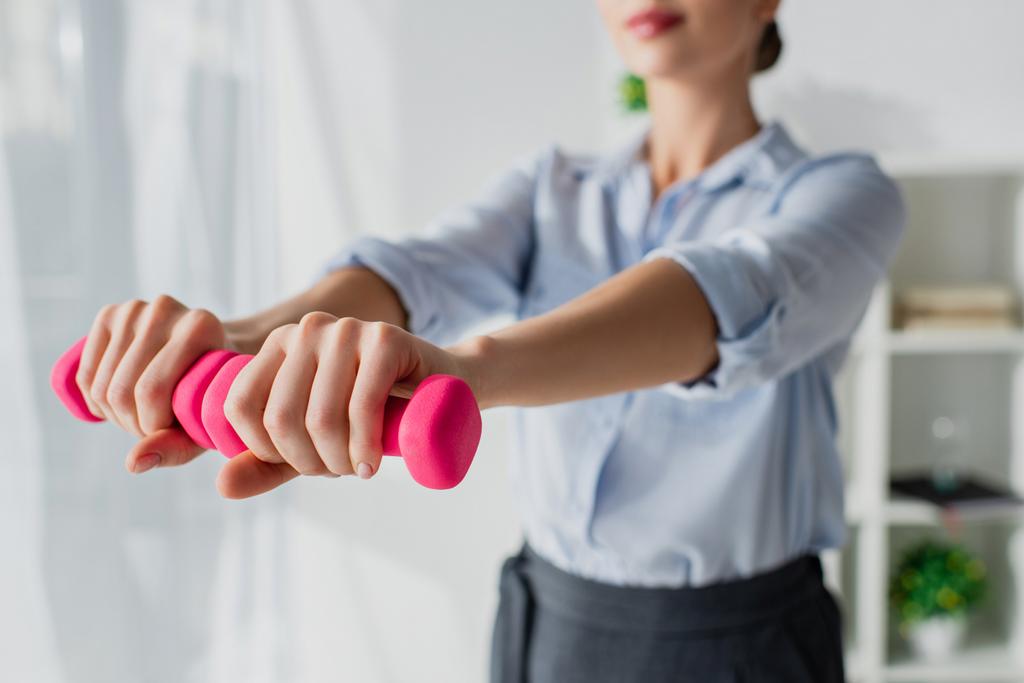 cropped view of businesswoman training with pink dumbbells in office, selective focus - Photo, Image