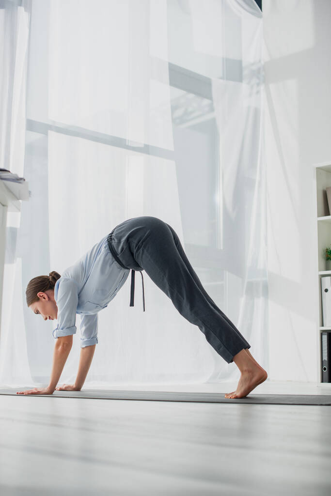 empresaria practicando yoga en postura Downward-Facing Dog sobre alfombra en oficina
  - Foto, Imagen