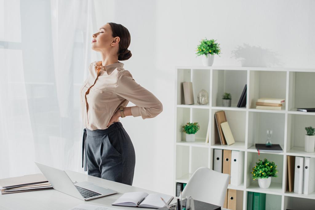 tired businesswoman stretching back at workplace in modern office - Photo, Image