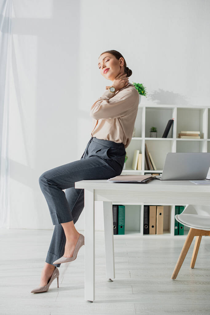 усталая деловая женщина растягивает шею на рабочем месте с ноутбуком
 - Фото, изображение