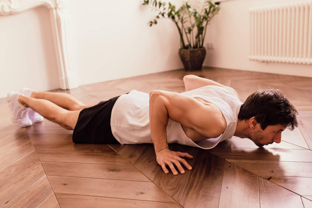 Lihaksikas urheilullinen sovi mies tekee push up harjoituksia kotona hänen valoisa huoneisto minimalistinen sisustus
 - Valokuva, kuva