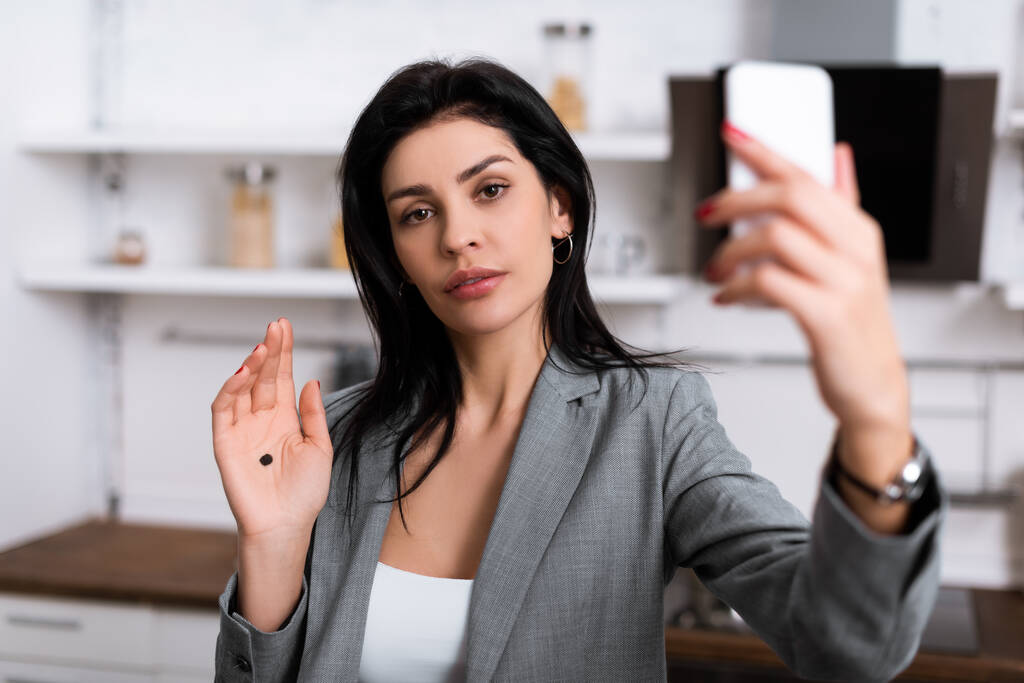 selective focus of attractive businesswoman with black dot on palm taking selfie, domestic violence concept  - Photo, Image
