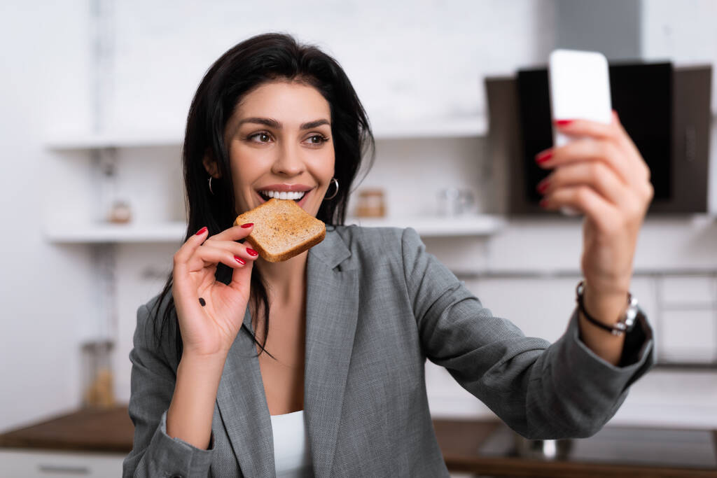επιλεκτική εστίαση του χαμογελαστού επιχειρηματίας με μαύρη κουκίδα στην παλάμη τρώει ψωμί τοστ και τη λήψη selfie, έννοια ενδοοικογενειακή βία  - Φωτογραφία, εικόνα