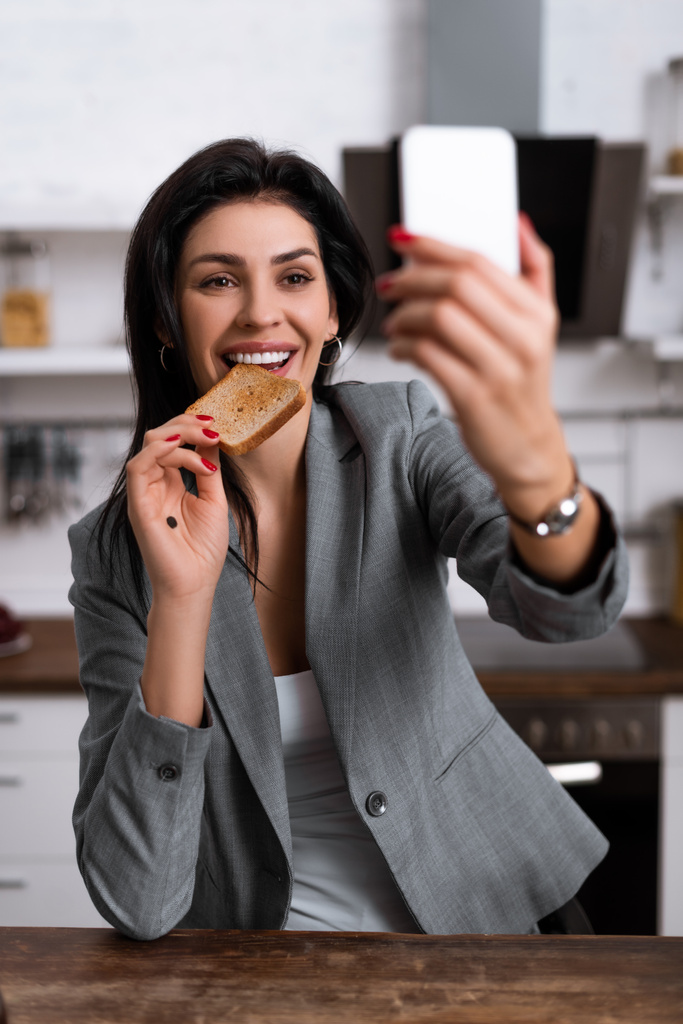 enfoque selectivo de la mujer sonriente con punto negro en la palma comer pan tostado sabroso y tomar selfie, concepto de violencia doméstica
  - Foto, Imagen