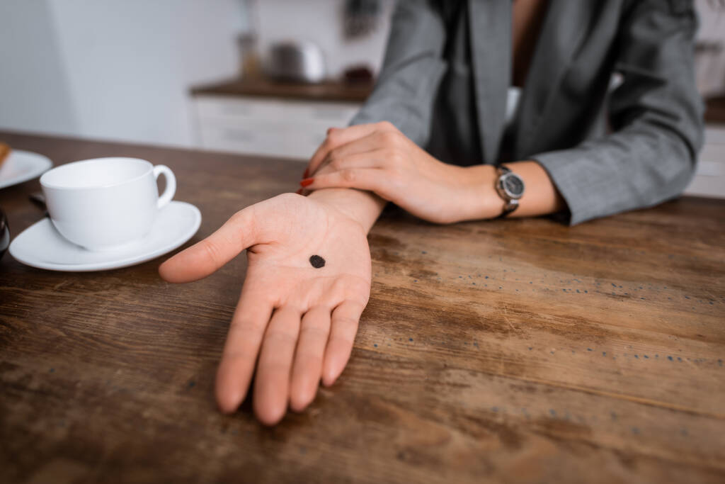 abgeschnittene Ansicht einer Frau, die Hand mit schwarzem Punkt auf der Handfläche in der Nähe einer Tasse zeigt, Konzept häuslicher Gewalt  - Foto, Bild