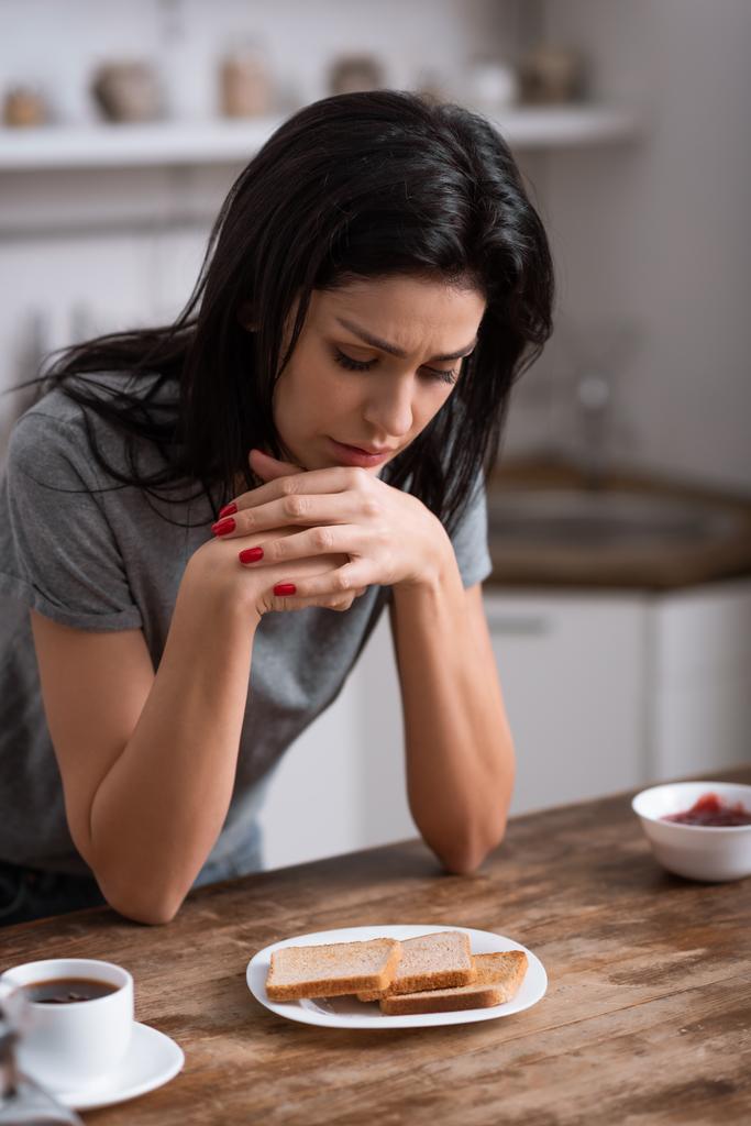 järkyttynyt nainen katselee lautasella paahtoleipää, perheväkivallan käsite
  - Valokuva, kuva
