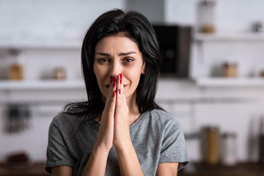 järkyttynyt nainen mustelmilla kasvoilla ja rukoilevat kädet itkien kotona, perheväkivallan käsite
  - Valokuva, kuva