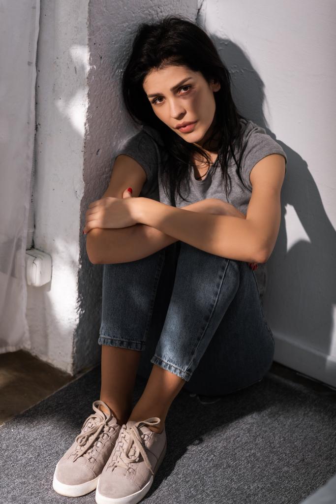 shadows on depressed woman with bruise on face and sitting on floor, domestic violence concept  - Photo, Image