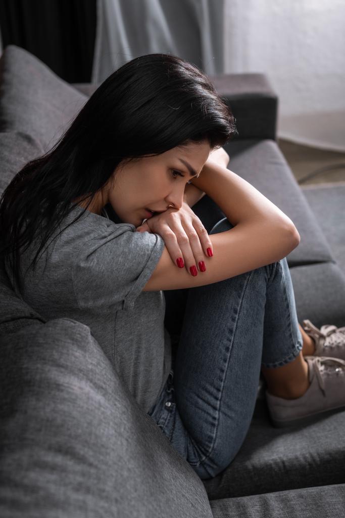 засмучена жінка в джинсах сидить на дивані, концепція домашнього насильства
  - Фото, зображення