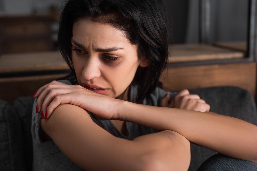 Frustrierte Frau mit blauen Flecken im Gesicht auf Sofa sitzend und wegschauend, Konzept häuslicher Gewalt  - Foto, Bild
