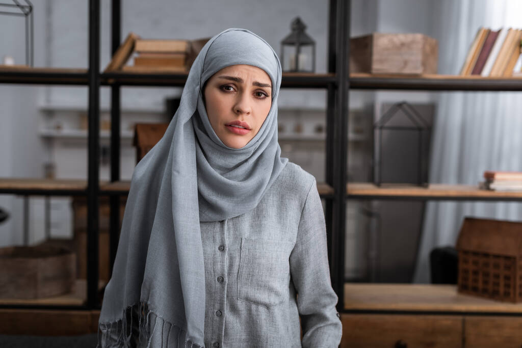 trieste moslim vrouw in hijab op zoek naar camera in de woonkamer, huiselijk geweld concept   - Foto, afbeelding