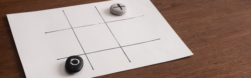 plan panoramique du jeu tic tac toe sur papier blanc avec des cailloux marqués de rien et croix sur la surface en bois
 - Photo, image