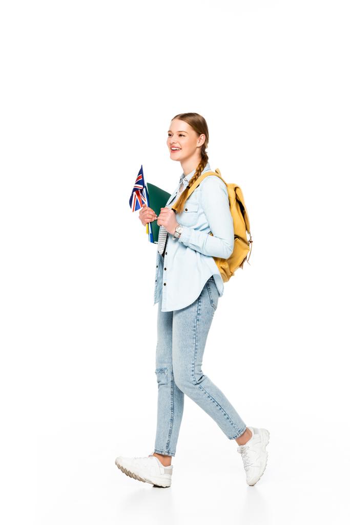 chica sonriente con trenza y mochila caminando con bandera de reino unido y copybooks aislados en blanco
 - Foto, Imagen
