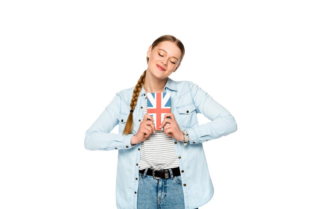 sonriente chica bonita con trenza y ojos cerrados sosteniendo libro con bandera del Reino Unido aislado en blanco
 - Foto, Imagen
