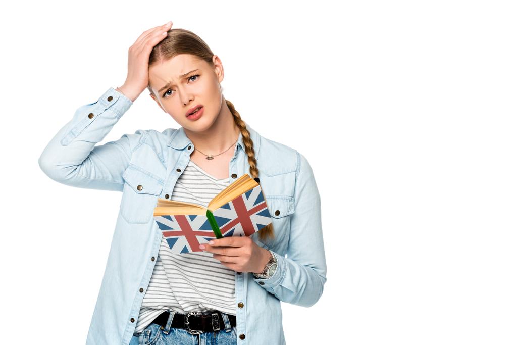 τεταμένη όμορφη κοπέλα με πλεξούδα βιβλίο ανάγνωσης με σημαία Ηνωμένο Βασίλειο και αγγίζοντας το κεφάλι απομονώνονται σε λευκό - Φωτογραφία, εικόνα