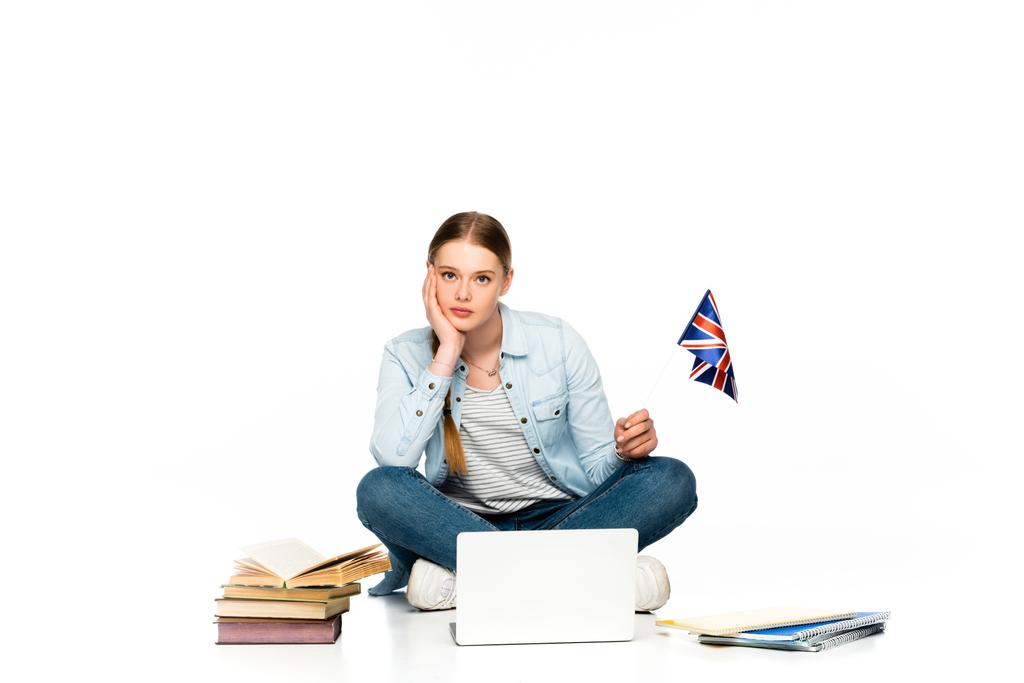 sad girl sitting on floor with laptop, books and copybooks and holding uk flag isolated on white - Photo, Image