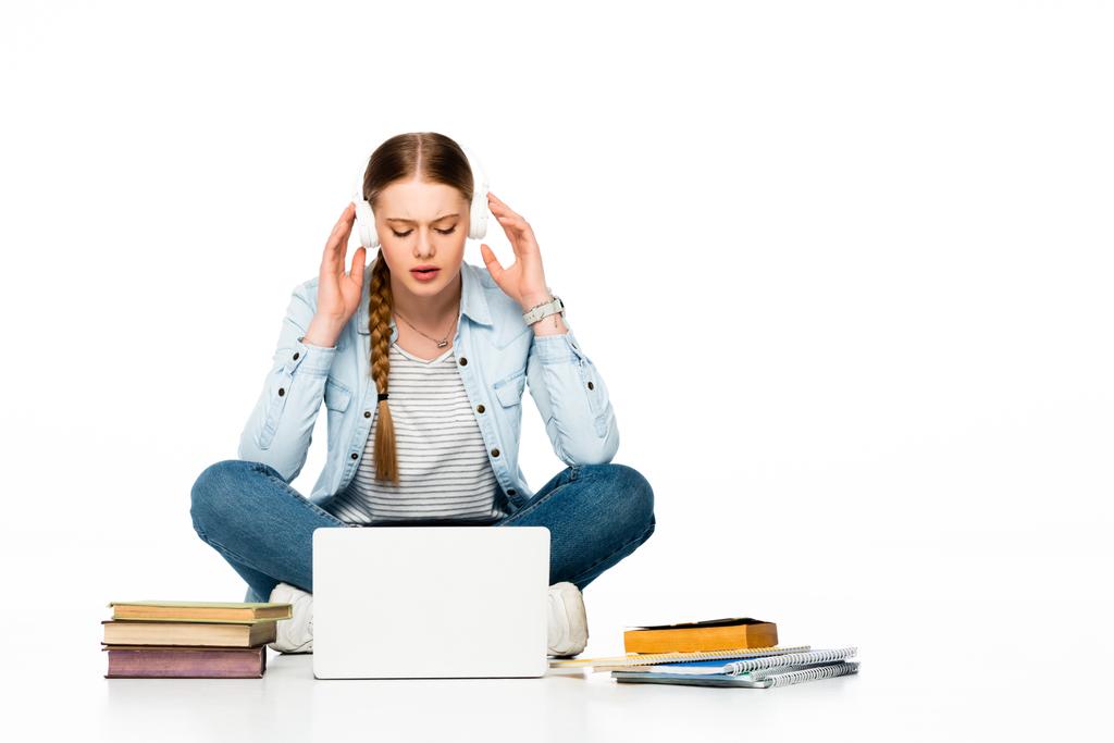 fille assise sur le sol dans des écouteurs près d'un ordinateur portable, livres et copybooks isolés sur blanc
 - Photo, image