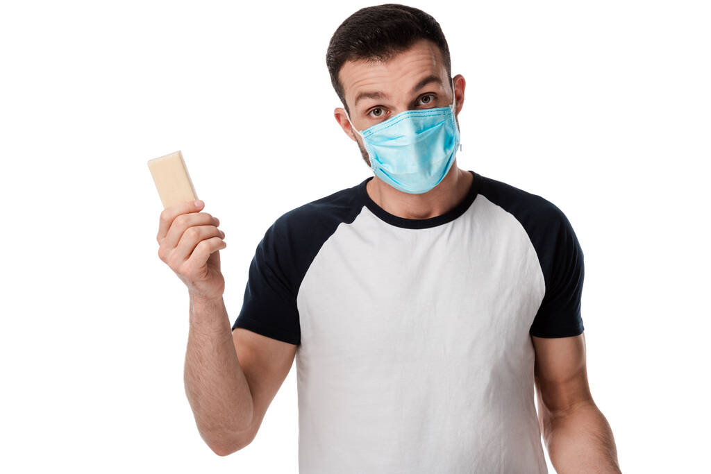 hombre en máscara médica sosteniendo barra de jabón y mirando a la cámara aislada en blanco
  - Foto, imagen