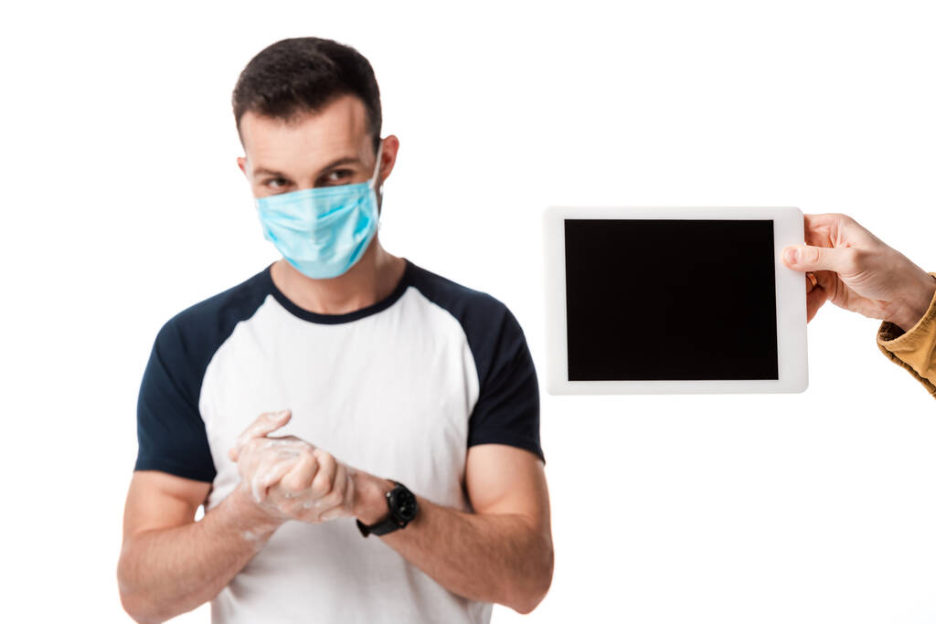 Mann in medizinischer Maske wäscht Hände in der Nähe von digitalem Tablet mit leerem Bildschirm isoliert auf weißem Hintergrund  - Foto, Bild