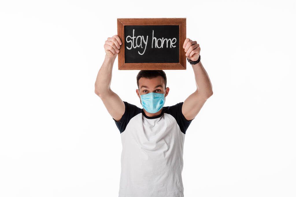 hombre en la máscara médica azul que sostiene el tablero de tiza con letras caseras de la estancia aisladas en blanco
  - Foto, imagen