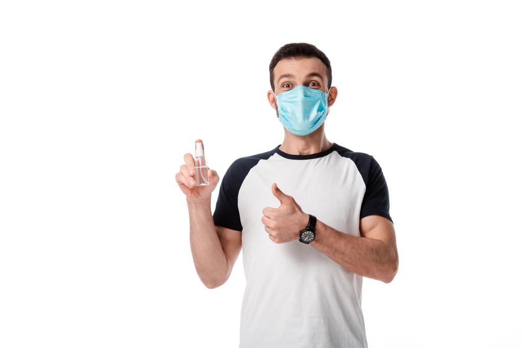 homem em máscara médica segurando frasco de spray com higienizador de mão e mostrando polegar para cima isolado no branco
  - Foto, Imagem