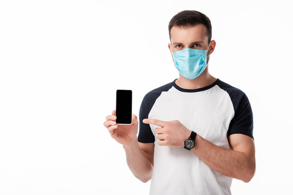 homme en masque médical pointant du doigt le smartphone avec écran blanc isolé sur blanc
  - Photo, image