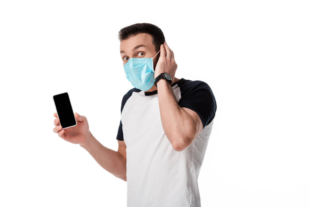 homem chocado em máscara médica segurando smartphone com tela em branco isolado no branco
  - Foto, Imagem