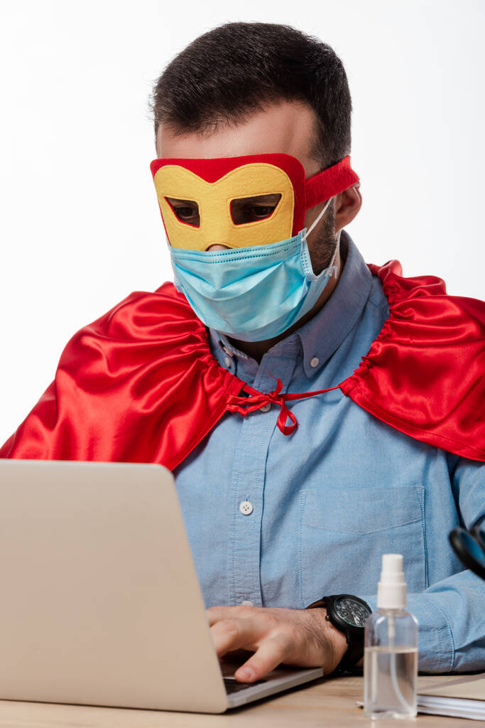 man met medisch masker en superheld cape met laptop geïsoleerd op wit  - Foto, afbeelding