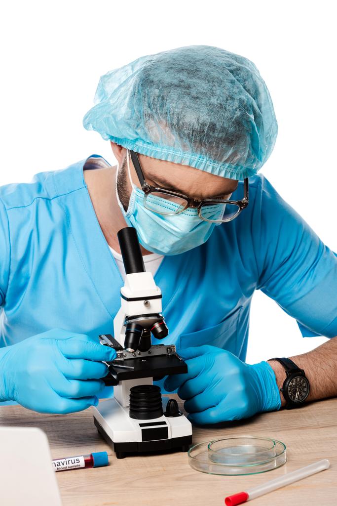 Wissenschaftler in medizinischer Mütze und Brille berühren Mikroskop in der Nähe von Reagenzgläsern mit Coronavirus Schriftzug isoliert auf weiß  - Foto, Bild