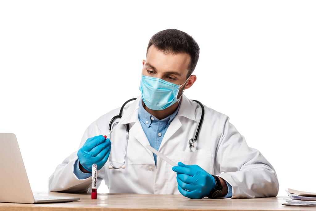 lékař v lékařské masce a bílém plášti se vzorkem krve s koronavirovým písmem izolovaným na bílém  - Fotografie, Obrázek