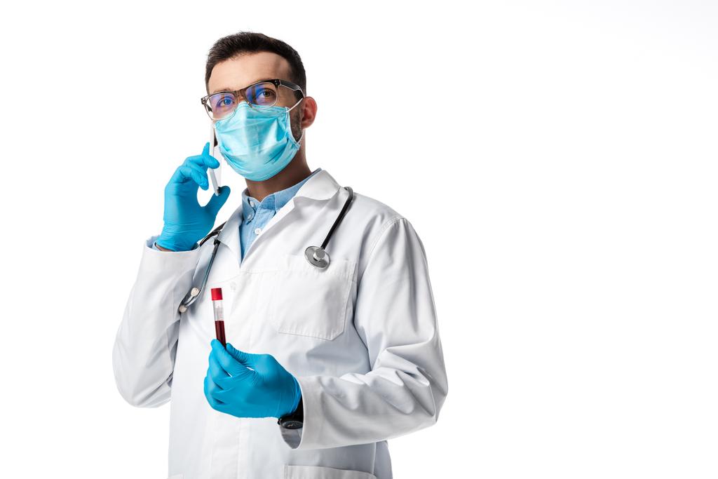 医療用マスクと白衣を着た医師がスマホで話しながら白衣に単離された血液サンプルを用いた検査管を持ち  - 写真・画像