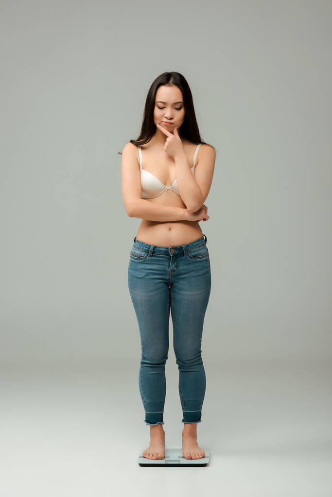 Düşünceli Asyalı aşırı kilolu kadın terazinin üzerinde duruyor ve gri düşünüyor. - Fotoğraf, Görsel