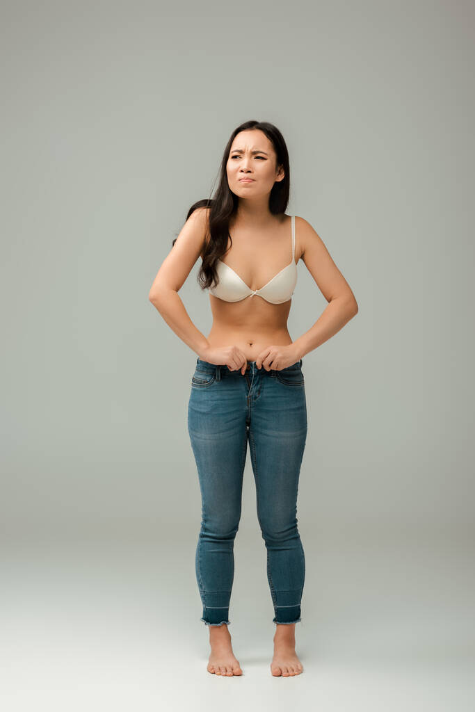 displeased and overweight asian girl wearing jeans on grey - Photo, Image