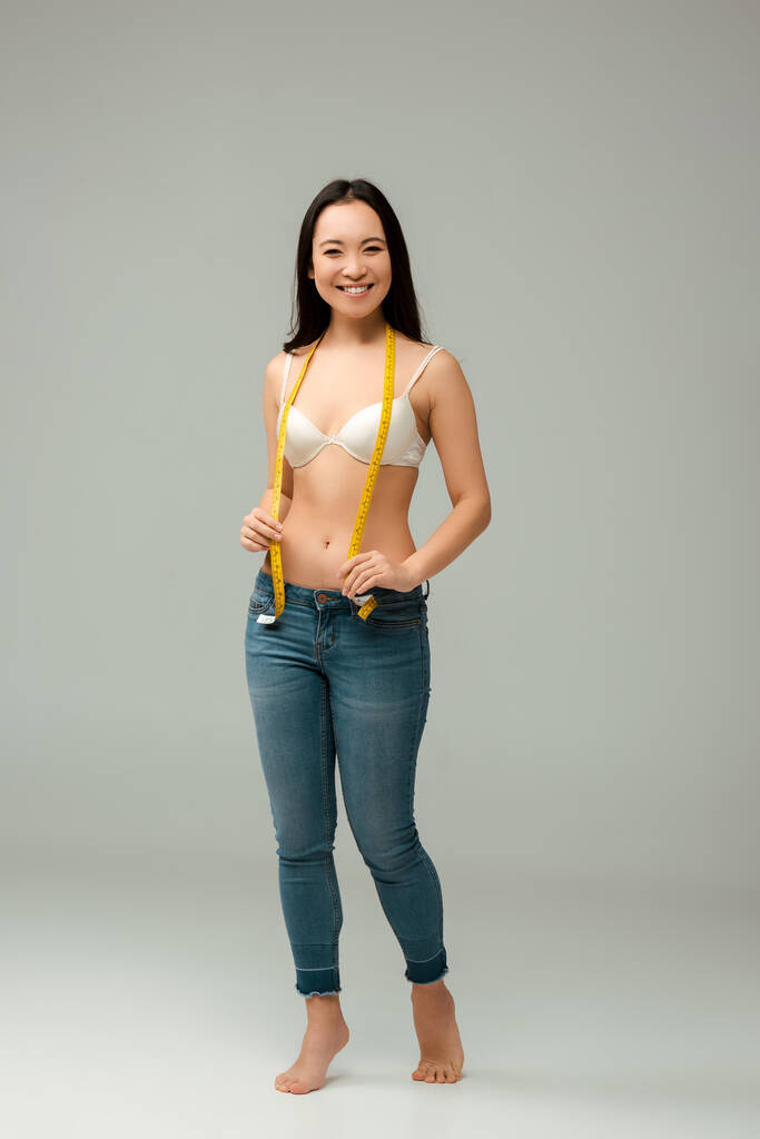 весела і надмірна вага азіатська дівчина тримає мірну стрічку на сірому
  - Фото, зображення