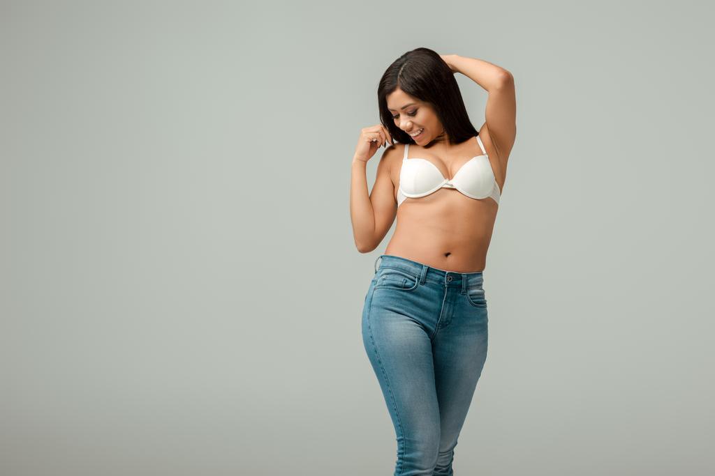 nadváha a šťastný africký Američan žena v džínách a podprsenka stojící izolované na šedé - Fotografie, Obrázek