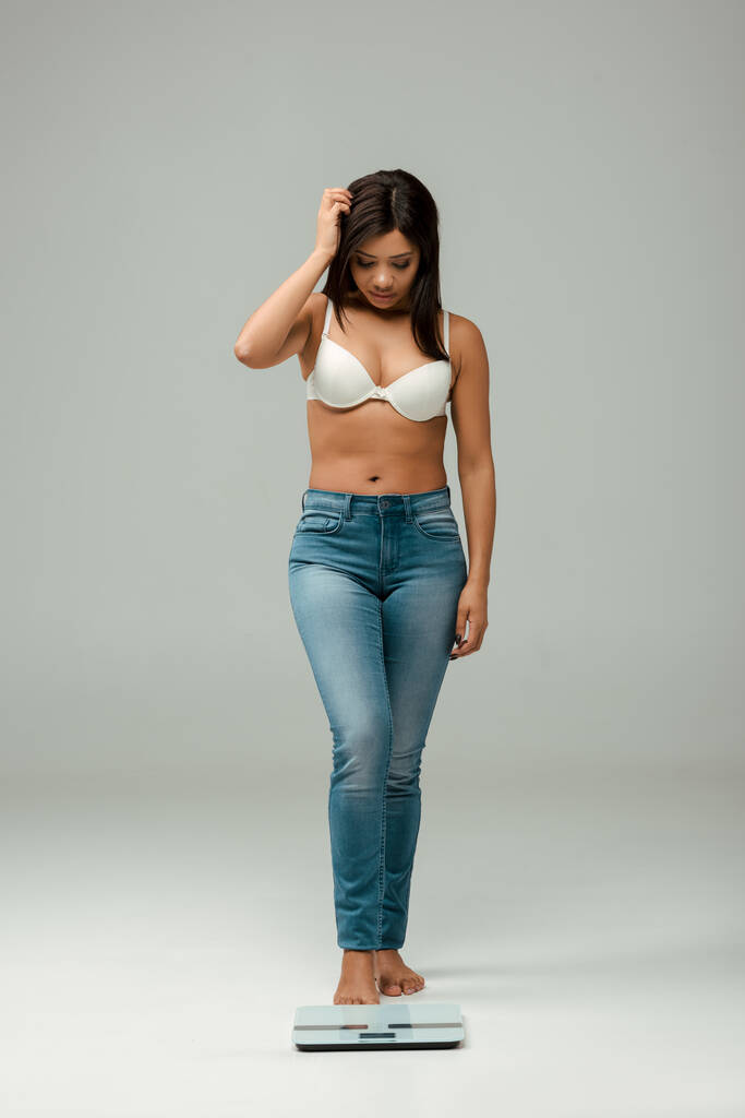 sobrepeso menina americana africana em jeans e sutiã olhando para escalas em cinza
 - Foto, Imagem